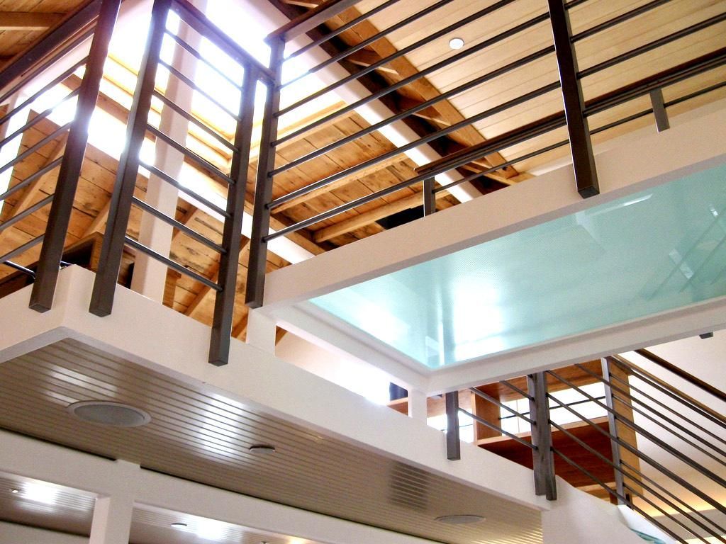 Modern interior with metal railings, glass floor panel, wood ceiling, and white walls.