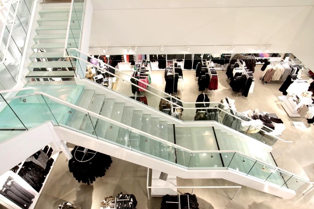 High-angle view of clothing store interior with glass staircases, clothing racks, and shoppers.