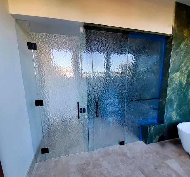 A modern bathroom shower with a textured glass door and sliding panel featuring black metal hardware.