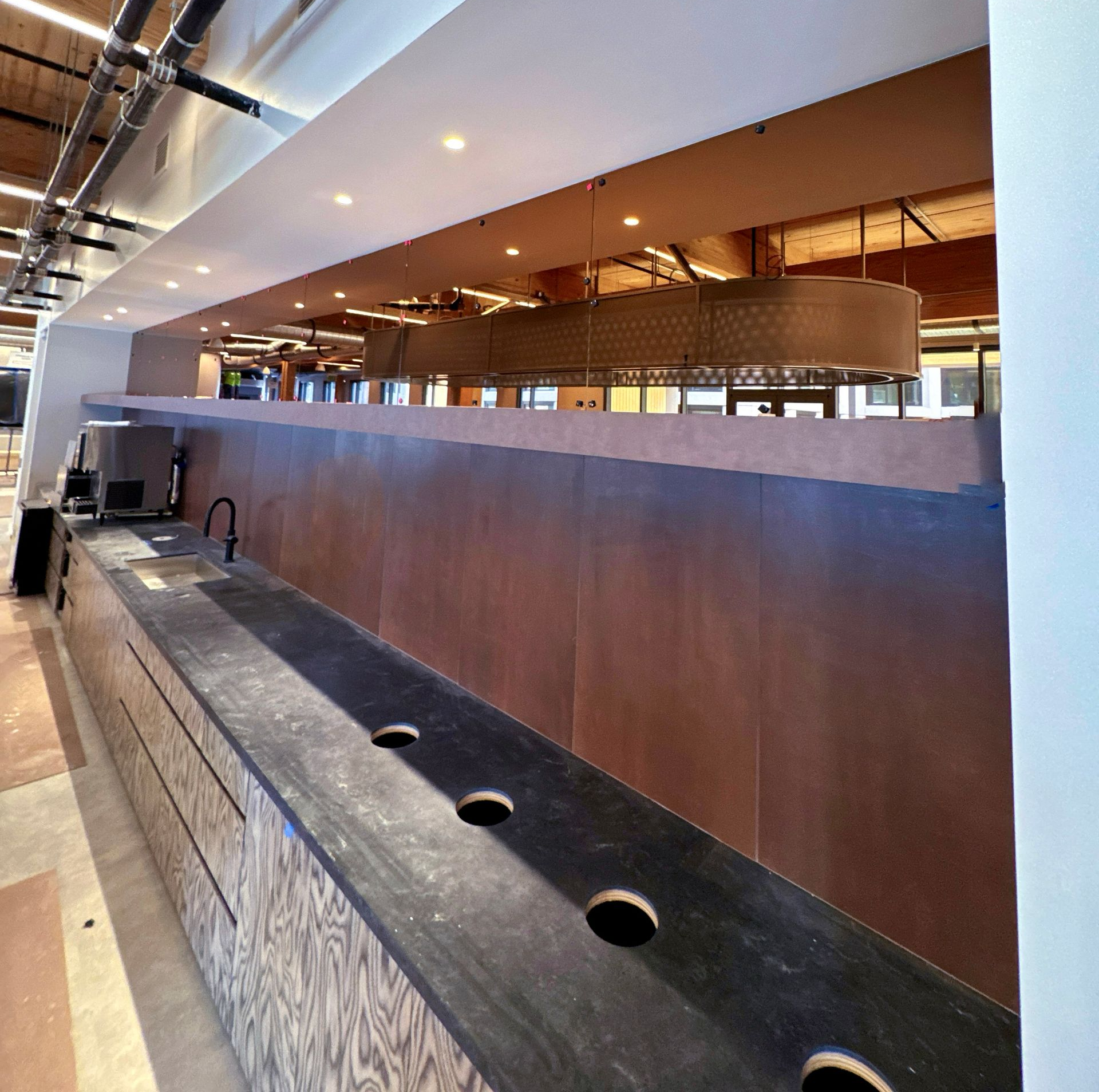 Long, dark countertop with round holes, a faucet, and a Copper colored mirror backsplash in a modern setting.