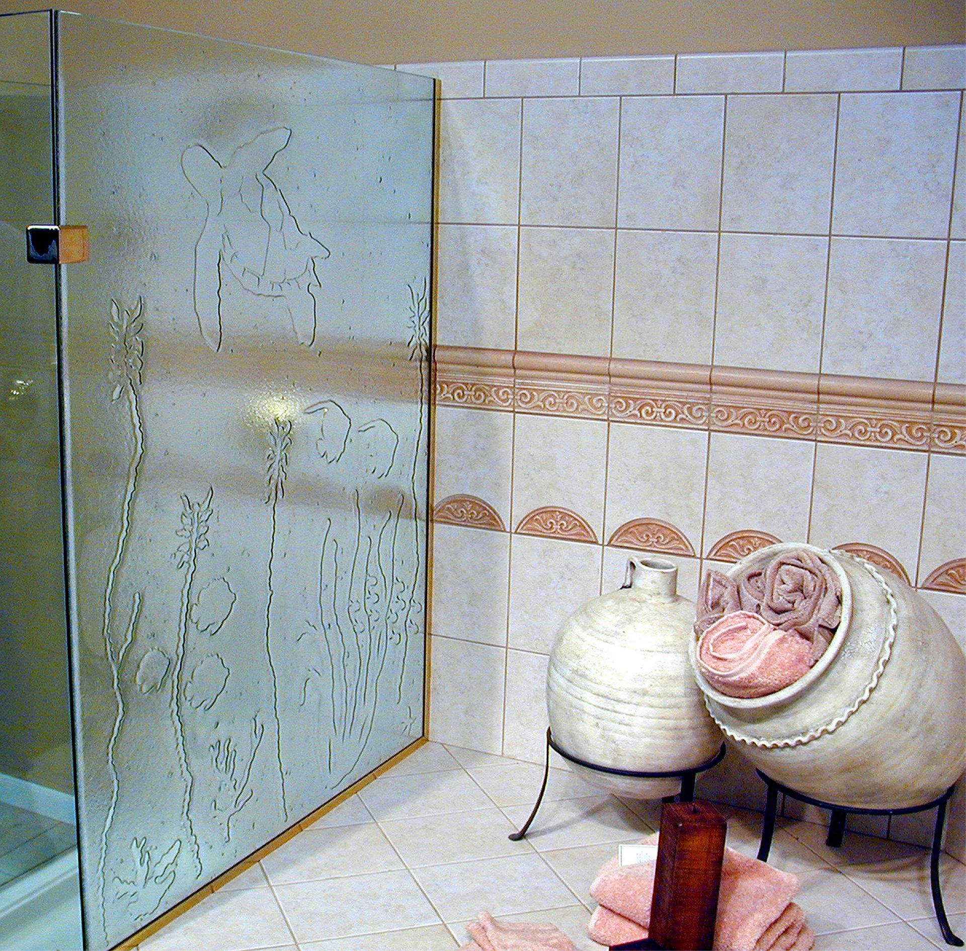 Shower stall with textured glass featuring sealife design; adjacent to tiles, decorative urns, and towels.