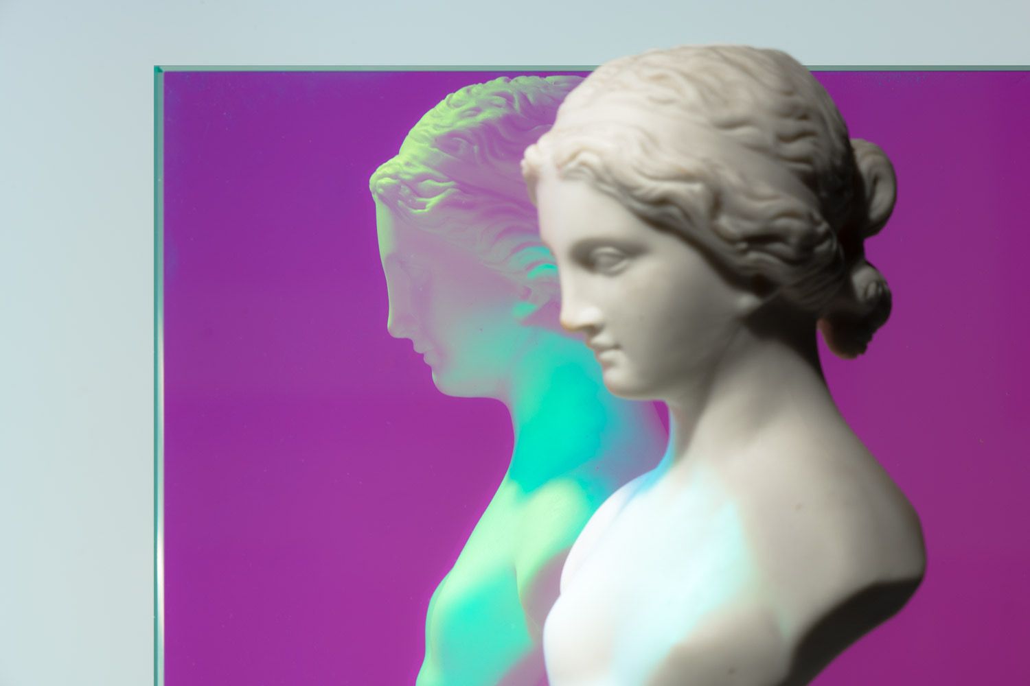 A white bust reflecting in a pane of dichroic glass showing purple and iridescent teal.