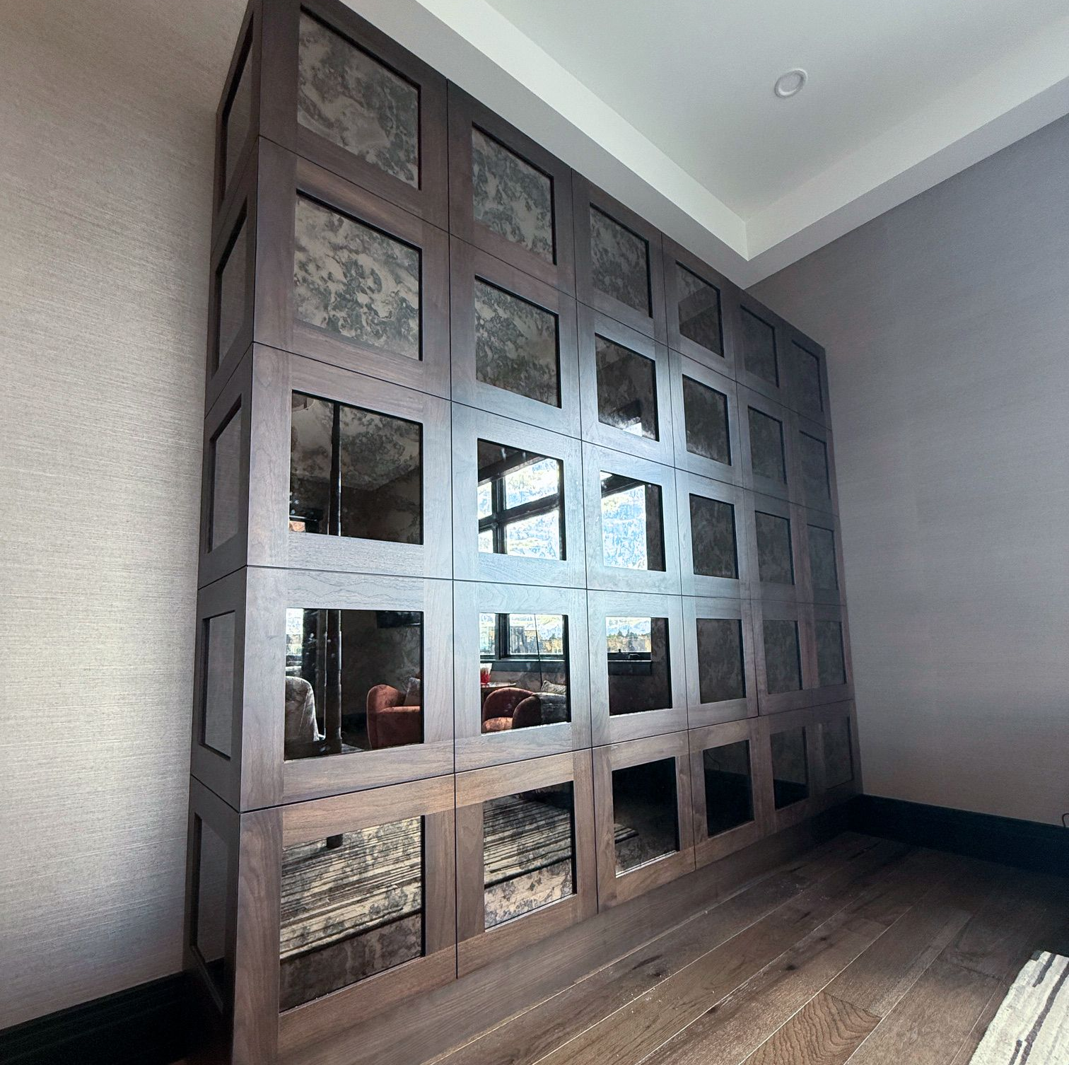 Large wooden closet with square bronze antique mirrored doors in a room with wood flooring and gray walls.