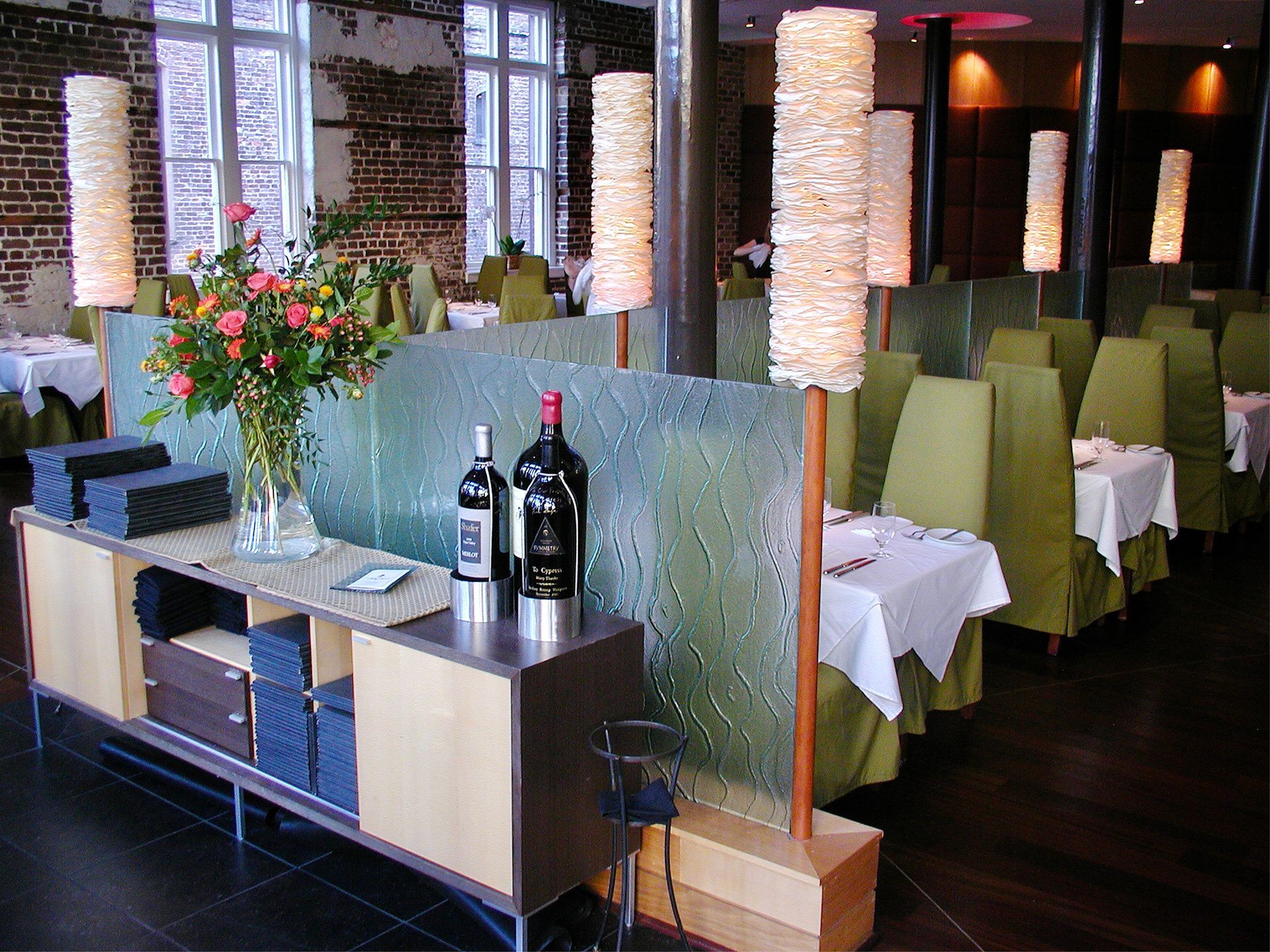 Upscale restaurant interior with tall lamps, green chairs, and tables set for dining.