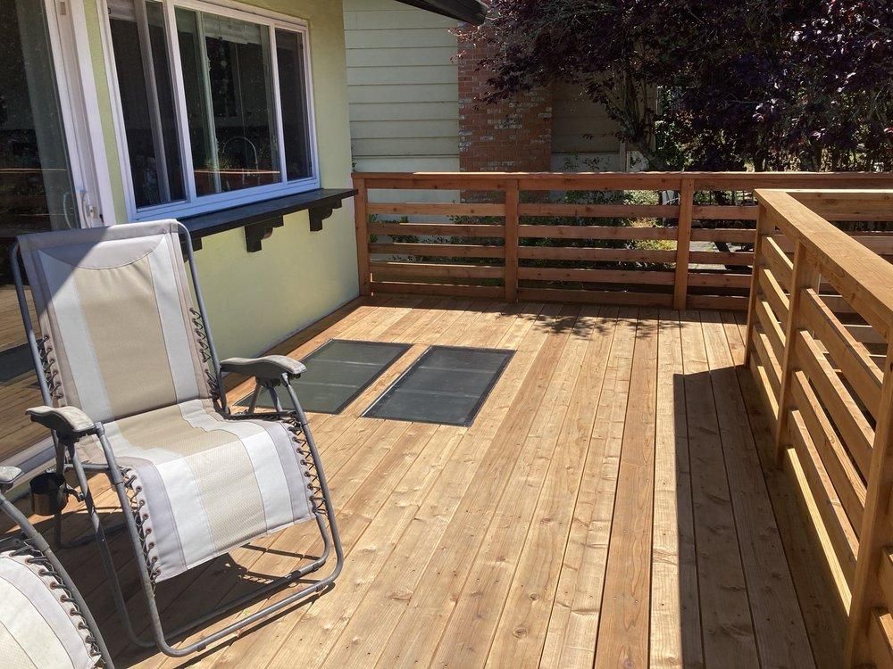 Wooden deck with lounge chairs, railing, and a window.