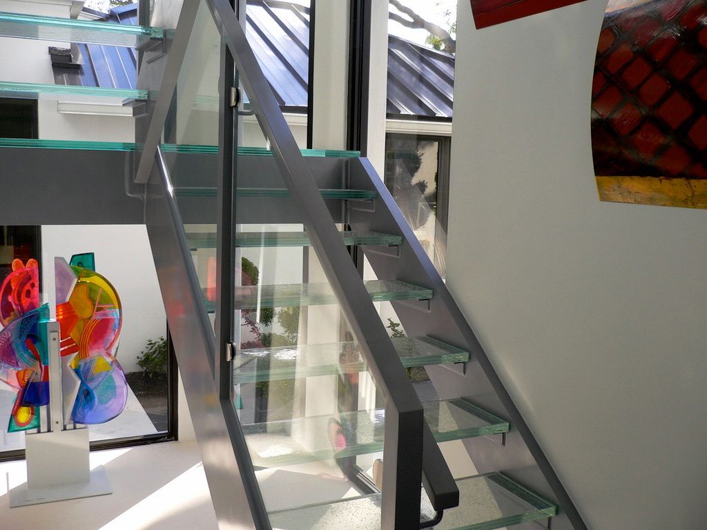 A staircase with a glass railing and a painting on the wall