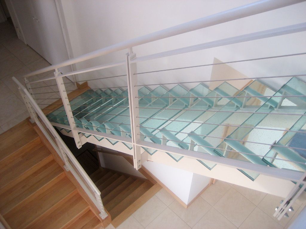Staircase with wooden steps, glass steps, and white metal railing. The glass creates a transparent effect.