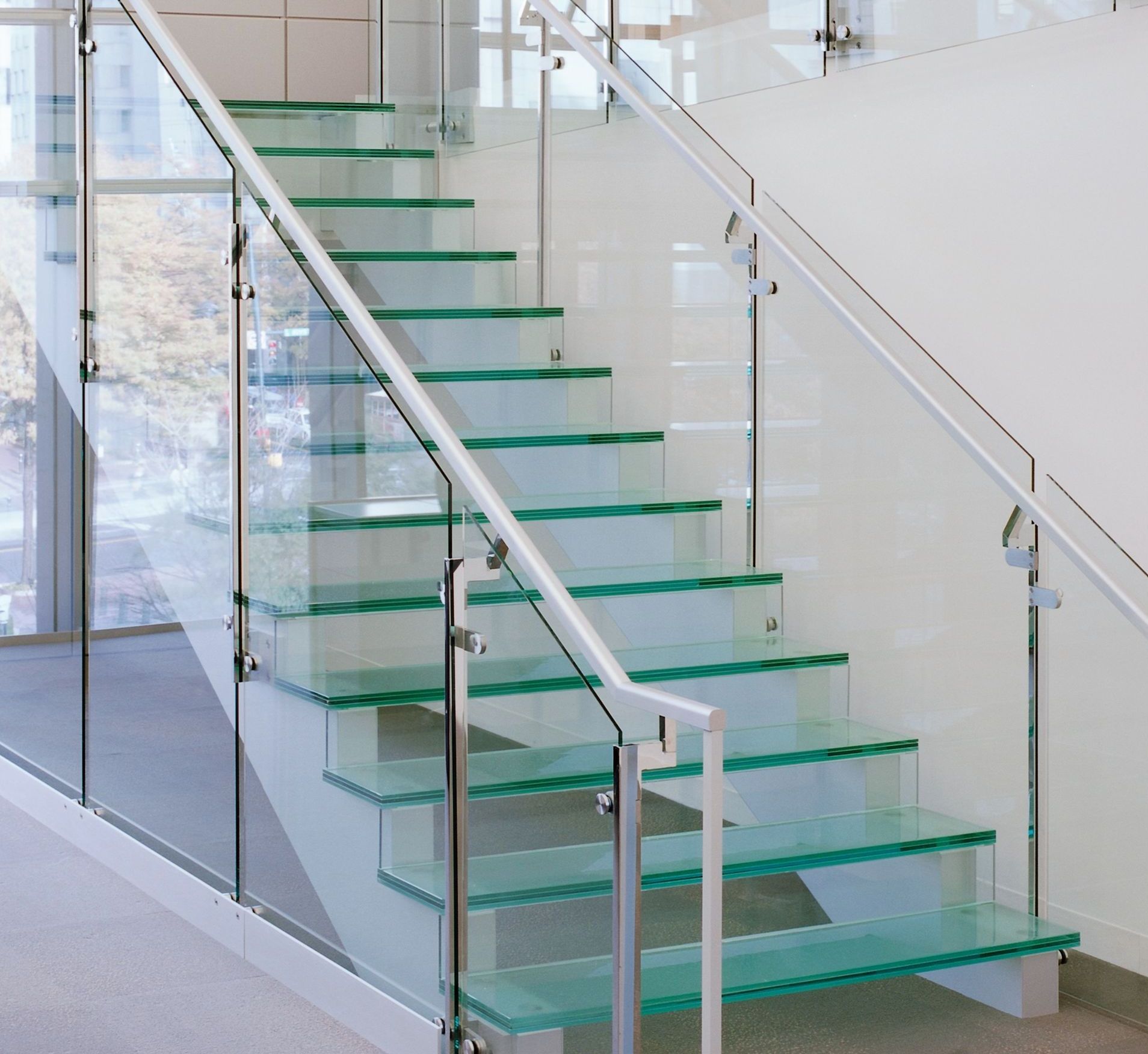 Glass staircase with glass steps and railing, set in a modern building. The steps have a slight green tint.