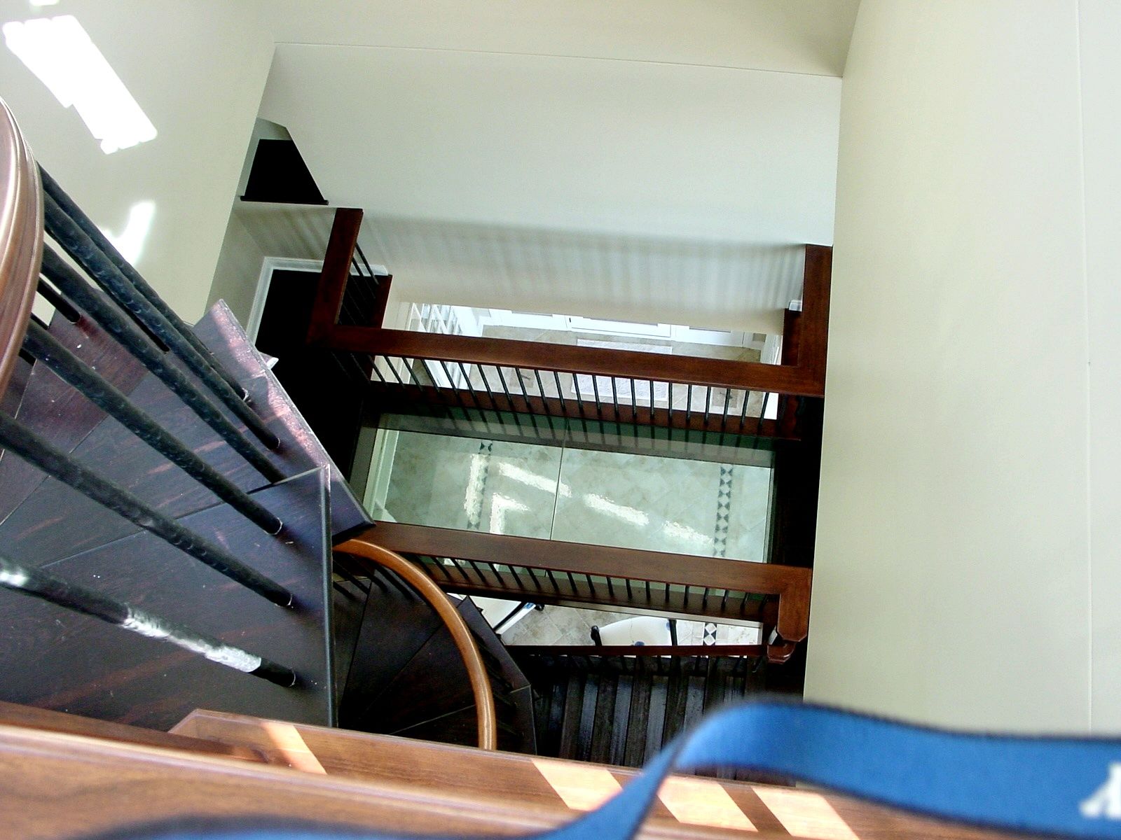 Stairwell viewed downward, with metal railings and bright sunlight on white walls.