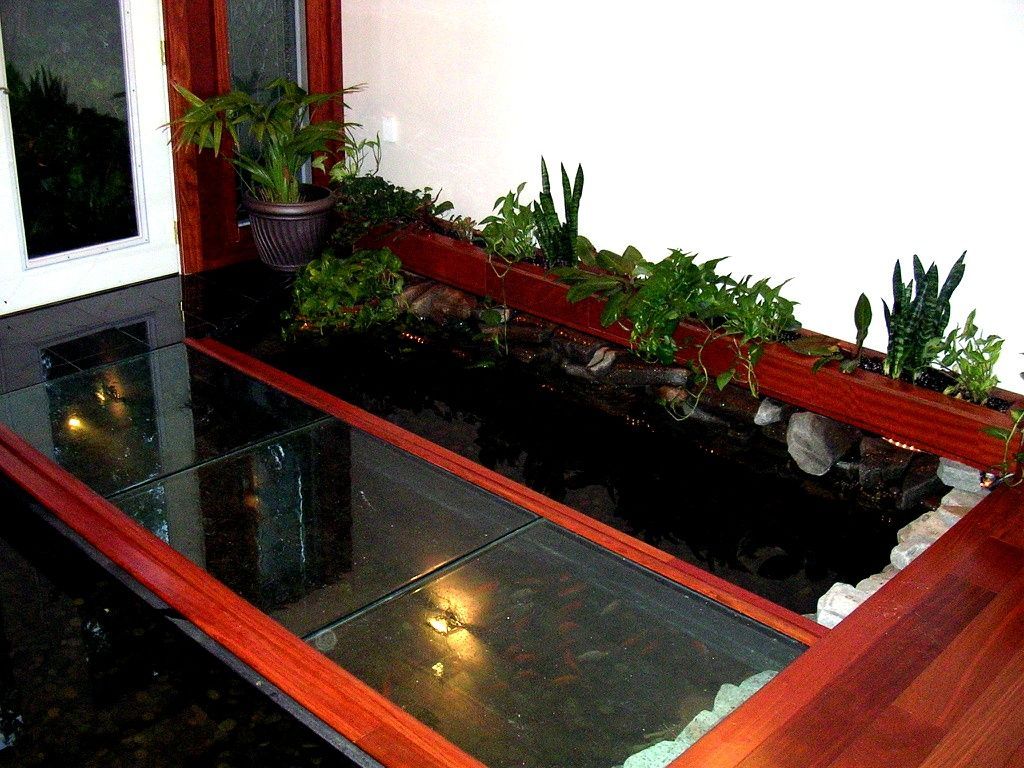 Indoor courtyard with red-trimmed rectangular pond, dark water, and potted plants along the edge