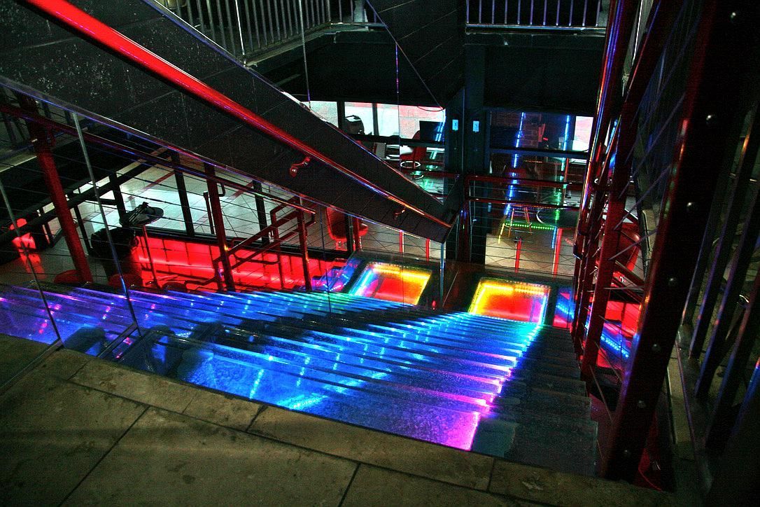 Staircase with vibrant blue and red lights illuminating the steps and handrails, leading downwards.