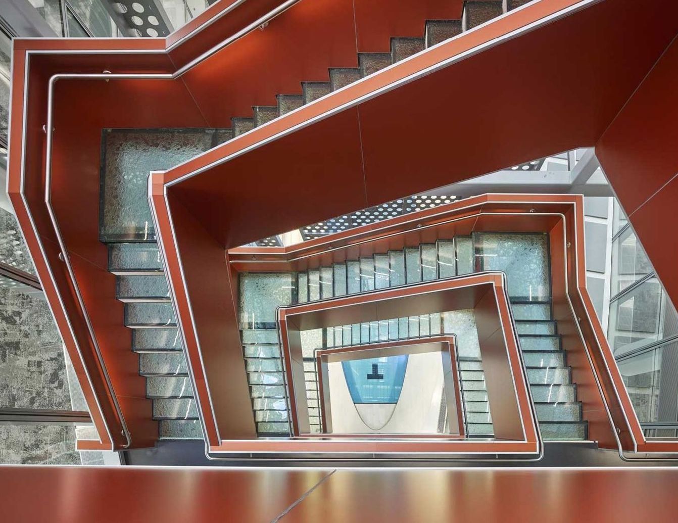 Overhead view of an abstract, rust-colored staircase with glass and white accents descending multiple levels.