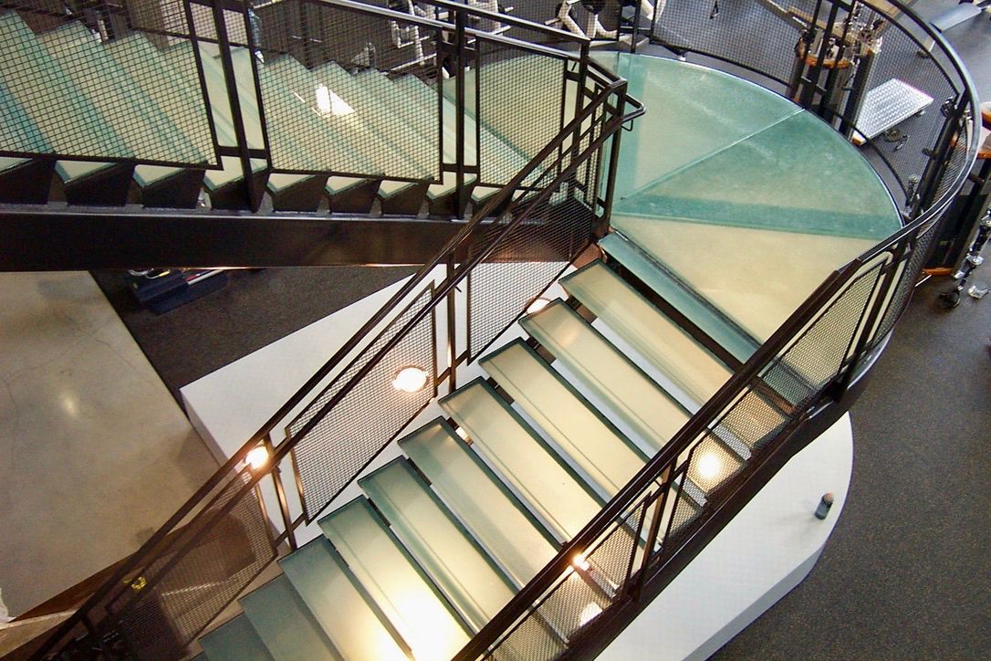 Curving staircase with glass steps and black metal railings in a modern interior.