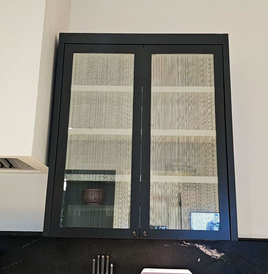 Black cabinet with glass doors mounted on a wall. The doors reflect the room.