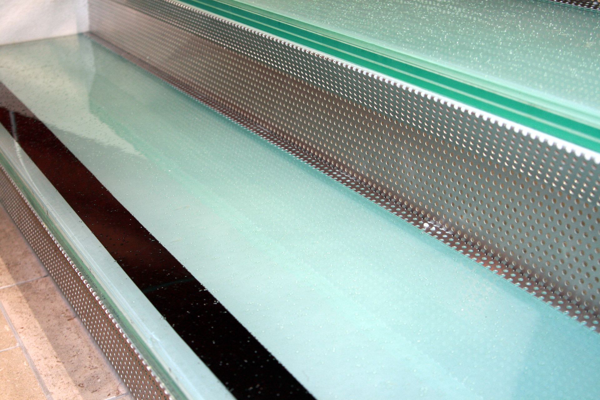 Close-up of glass panels with a perforated metal layer, featuring a black stripe.