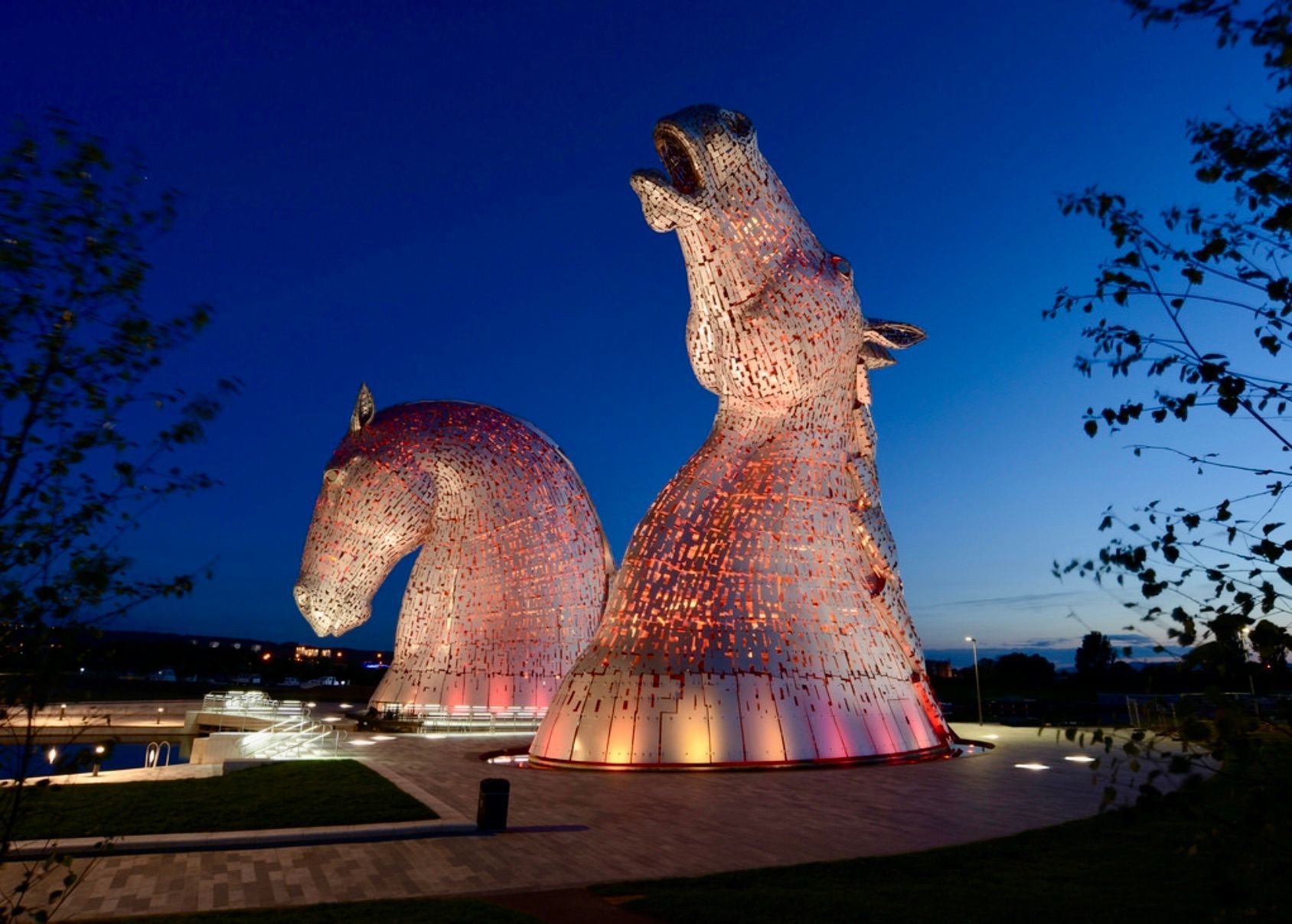 Two illuminated Kelpies sculptures at night, glowing pink and orange.