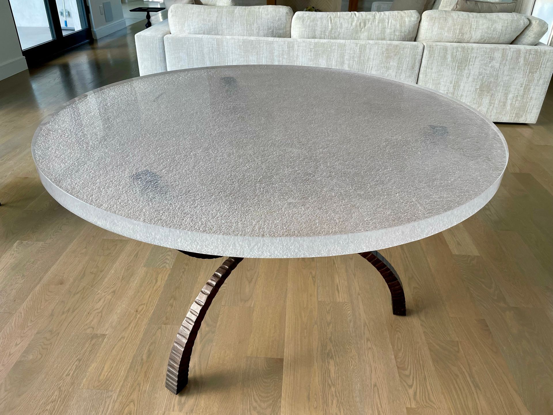 A round glass table is sitting on a wooden floor in a living room next to a couch.