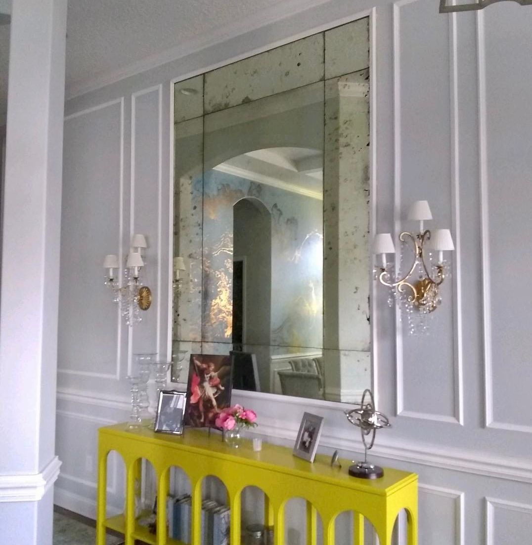 A hallway with a yellow table and a large antique mirror