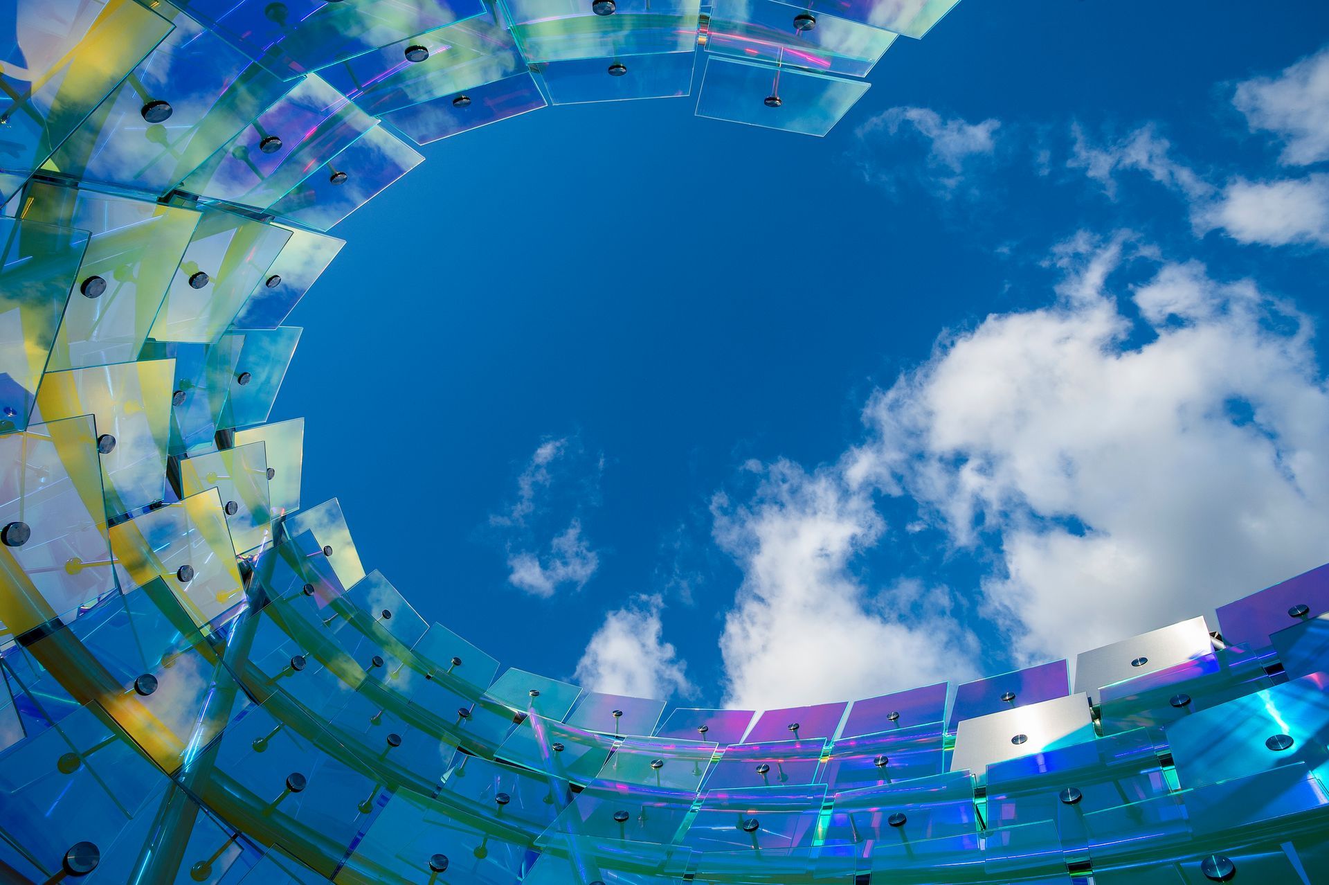 Circular mosaic sculpture framing a blue sky with white clouds