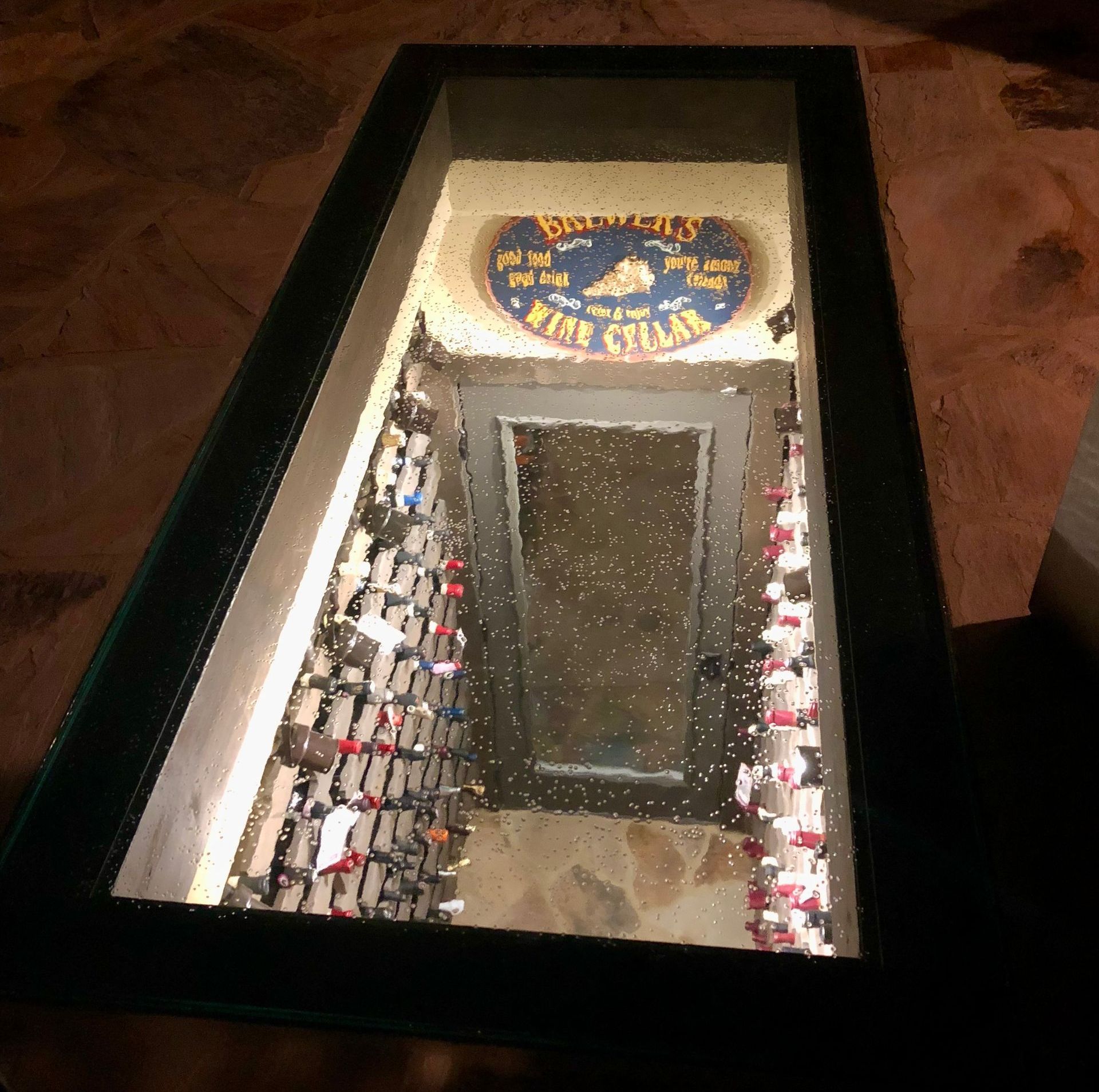 Glass-covered wine cellar entrance with rows of wine bottles. The sign says 