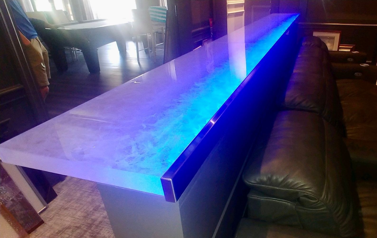 A long glass table top with blue lights on it is in a living room next to a couch.