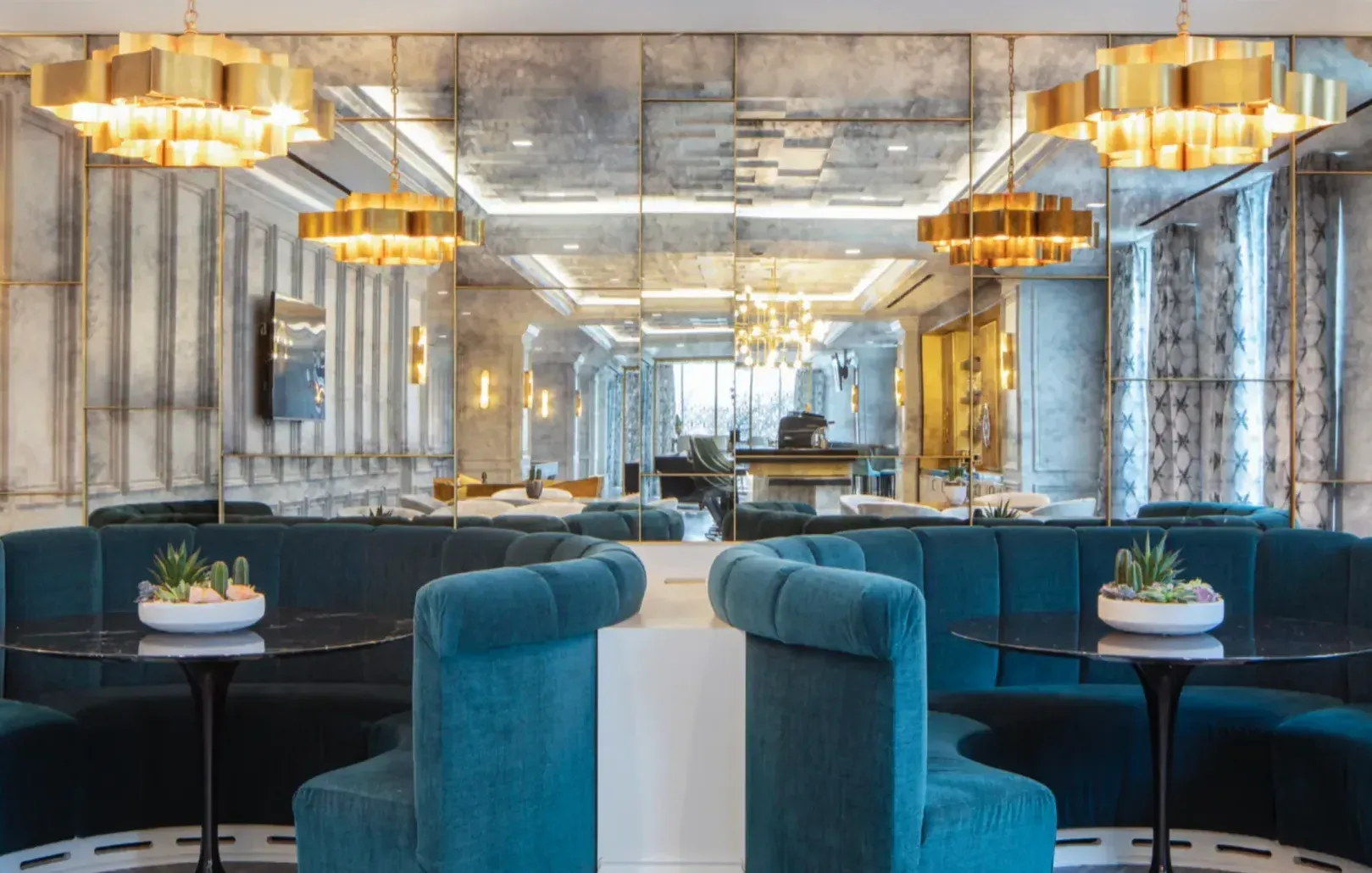 Restaurant interior with teal booths, gold light fixtures, and mirrored walls.
