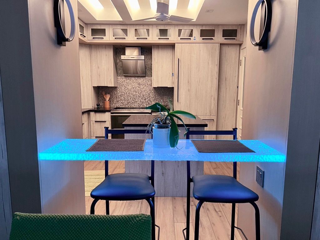 Kitchen with breakfast bar illuminated in blue light, facing cabinets and appliances.