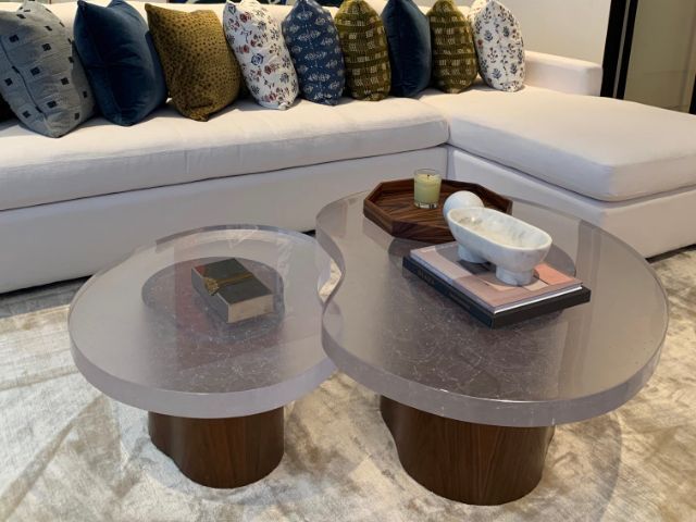 Two thick glass coffee tables on wooden bases with decor in front of a white sectional sofa.