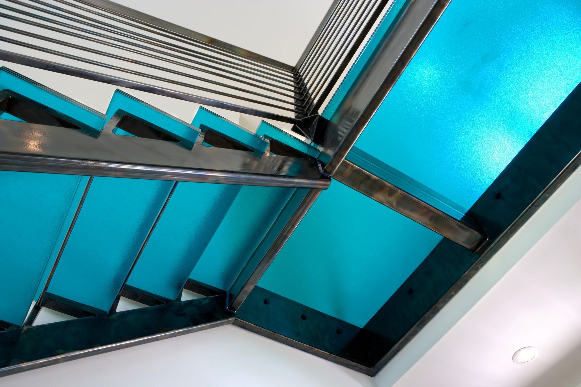 Staircase with turquoise treads, metal railings, and a white wall. Angled perspective.