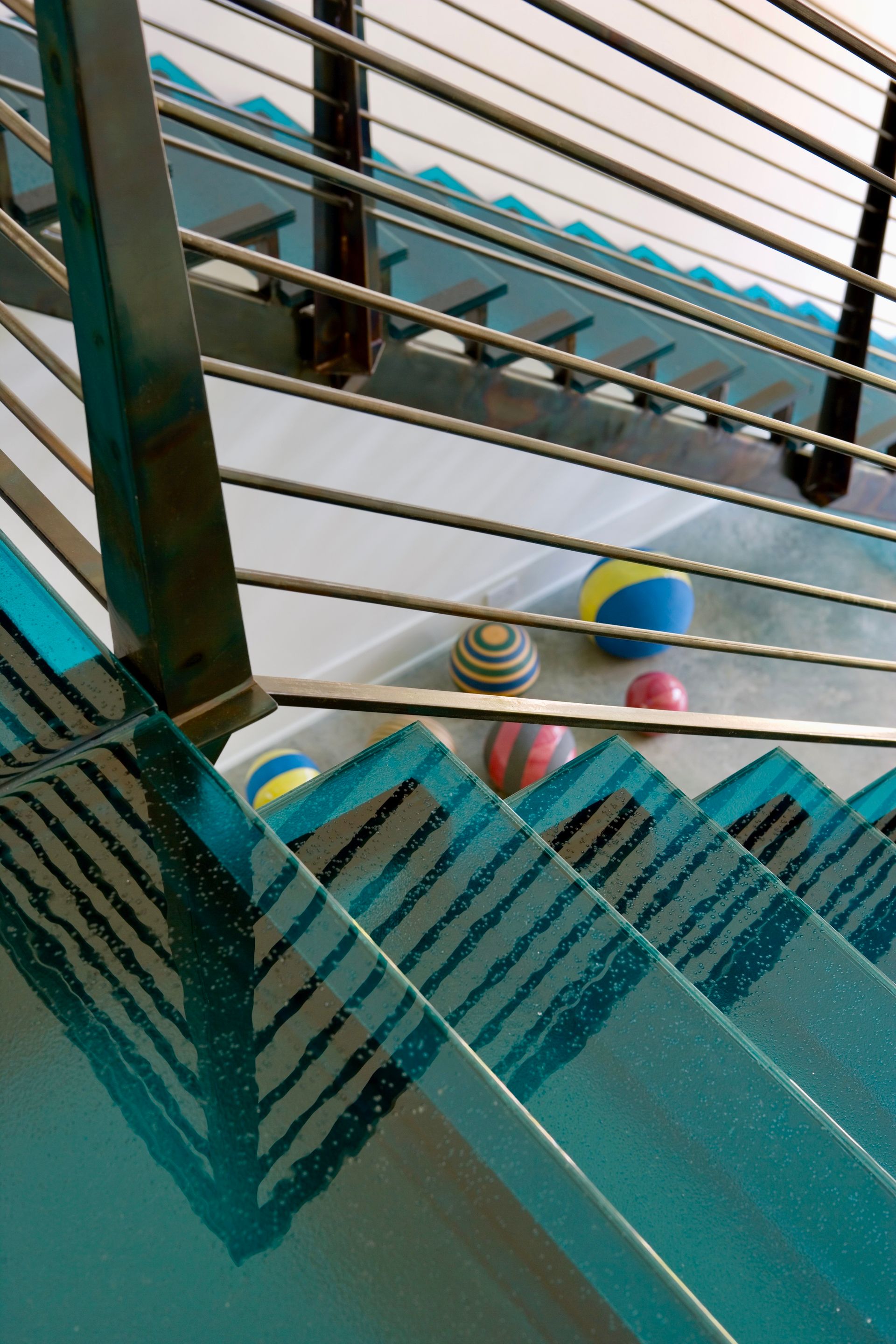 Glass staircase with blue accents and stainless steel railing; several balls on the steps.