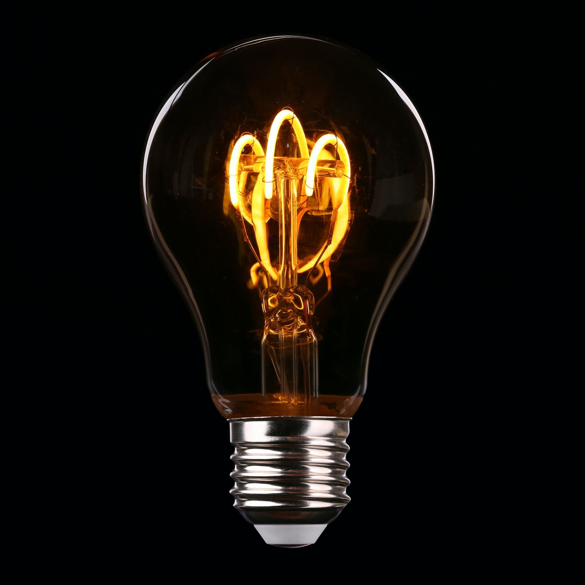 A lightbulb with a glowing filament set on a black background