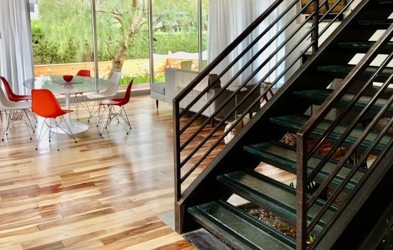 A dining area with a round glass table and orange chairs, next to an industrial-style metal staircase in a modern home.