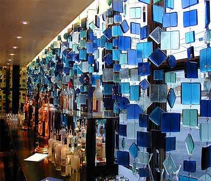 Bar with a hanging curtain of blue and clear glass tiles, bottles lining the bar.