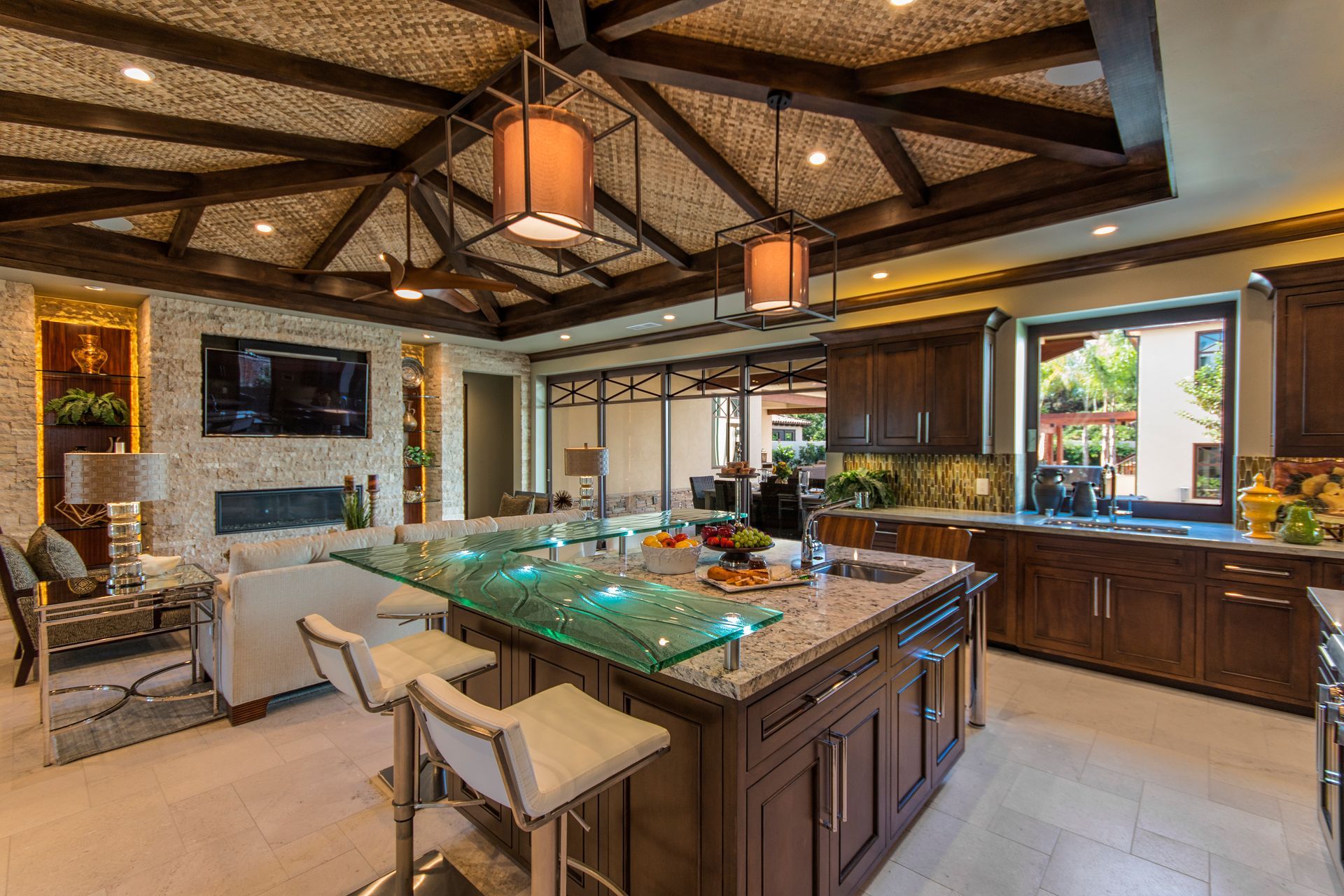 A luxury kitchen with dark wood cabinets, a glass-topped granite island with bar stools, and a textured beamed ceiling.