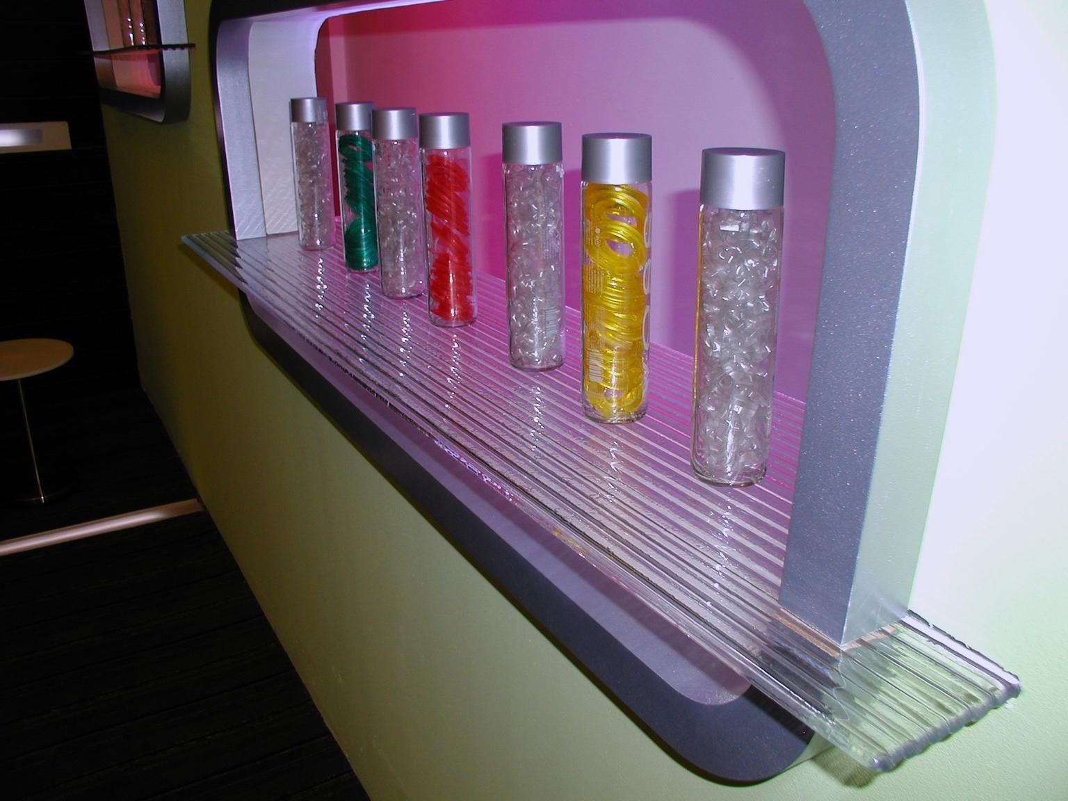 Seven vials with colorful contents on a ledge. Each vial has a silver cap.