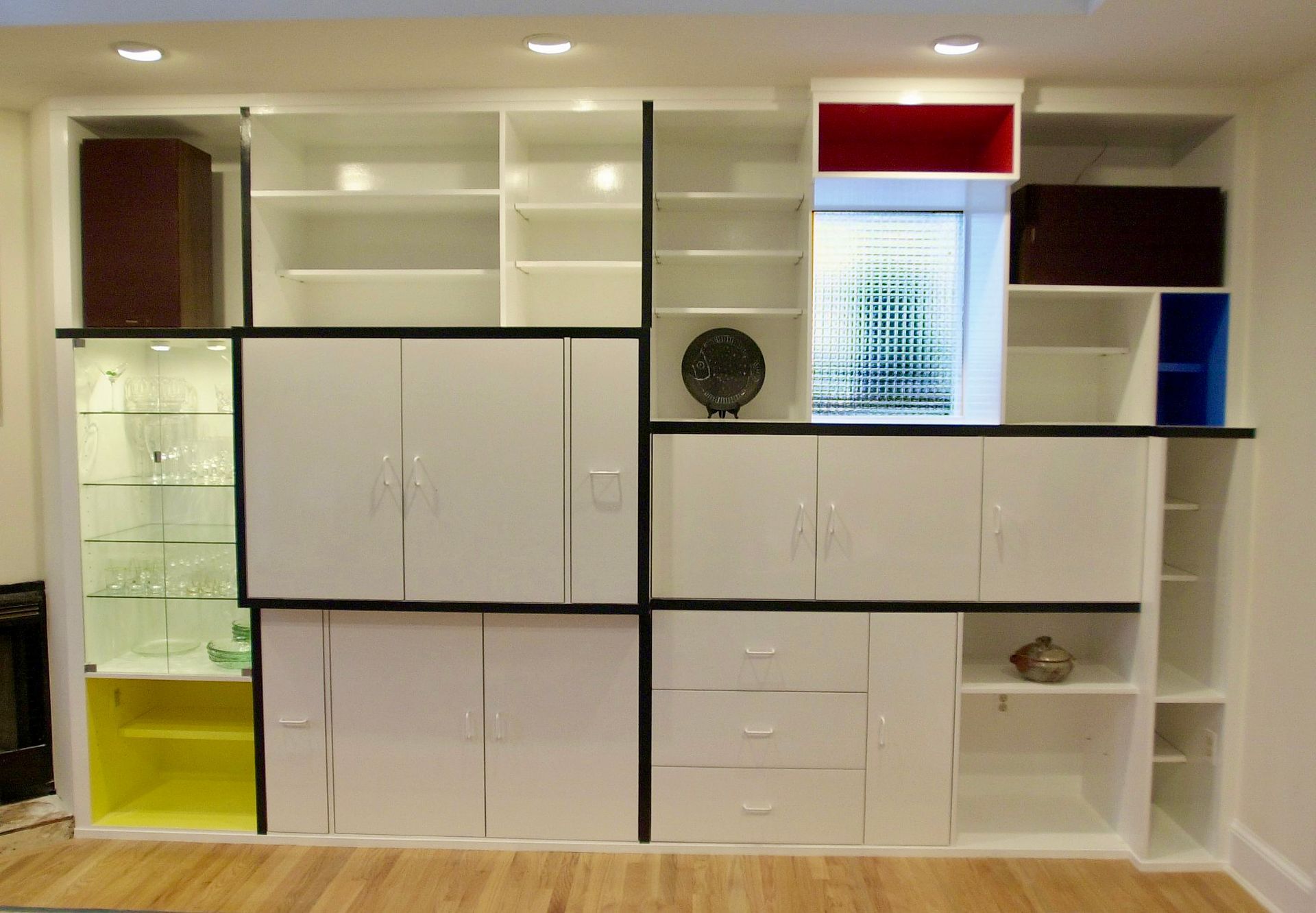 Large custom built-in white shelving unit with black trim, glass display cabinet, and colorful red, yellow, and blue accents.
