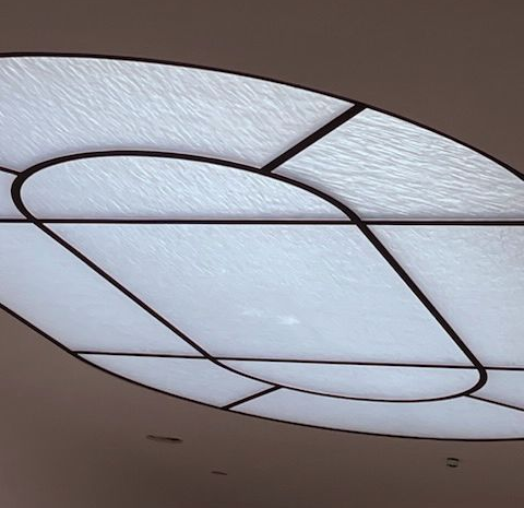 Oval, backlit ceiling panel with black geometric lines dividing textured white glass.