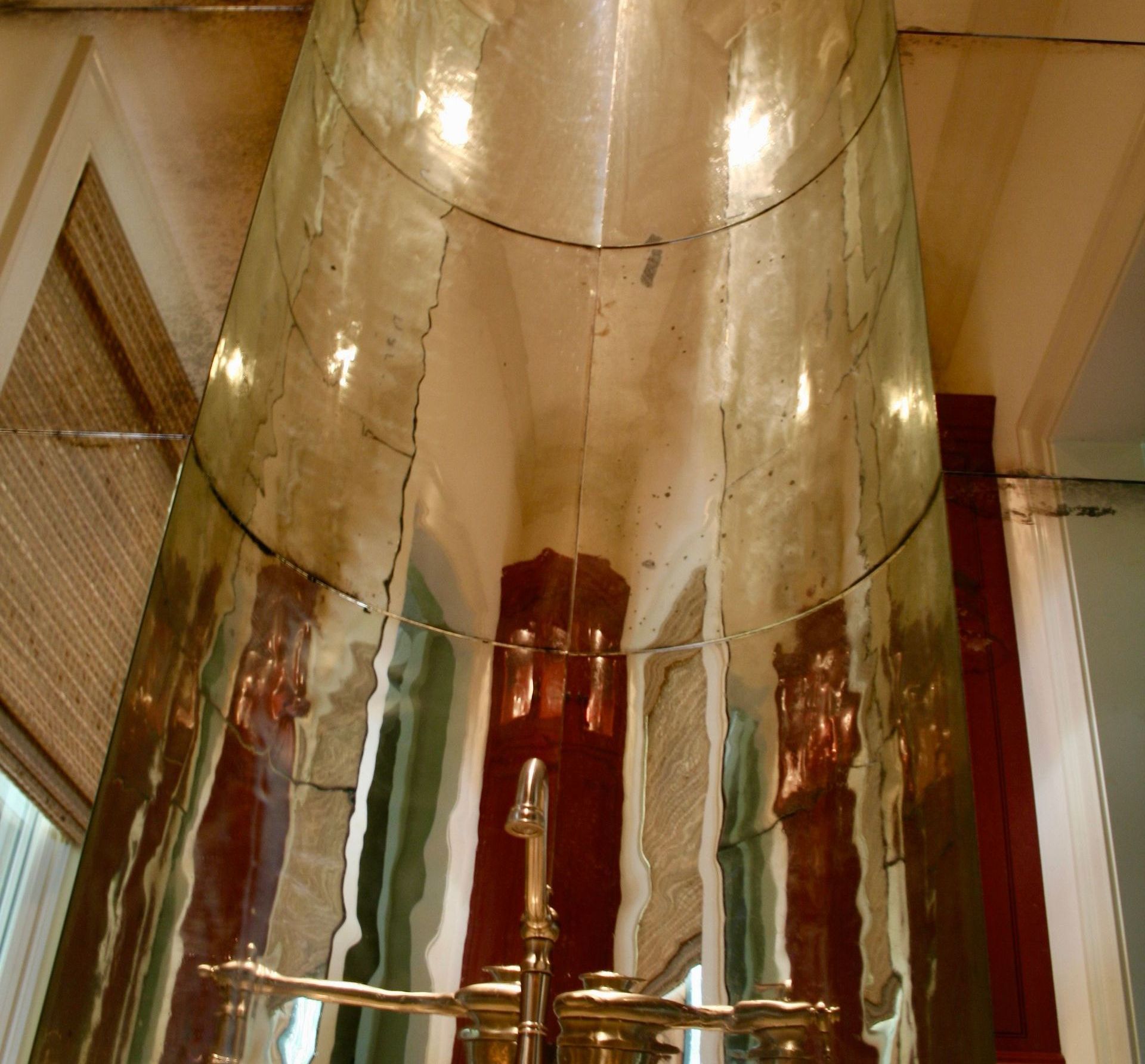 A very tall slumped mirror with a faucet attached to it