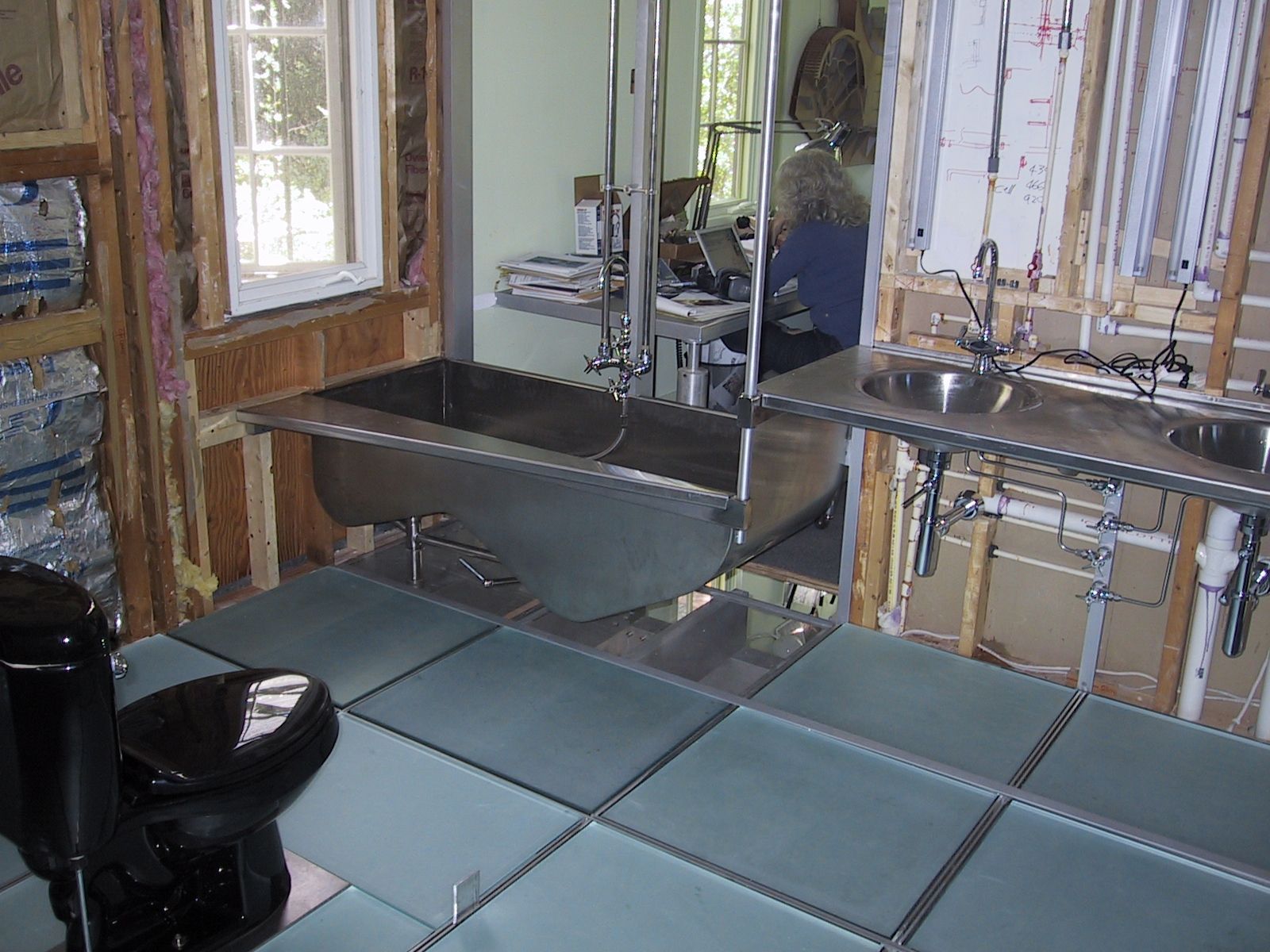 Bathroom renovation: Stainless steel fixtures, unfinished walls, a bathtub, sink, and a toilet on a tiled floor.