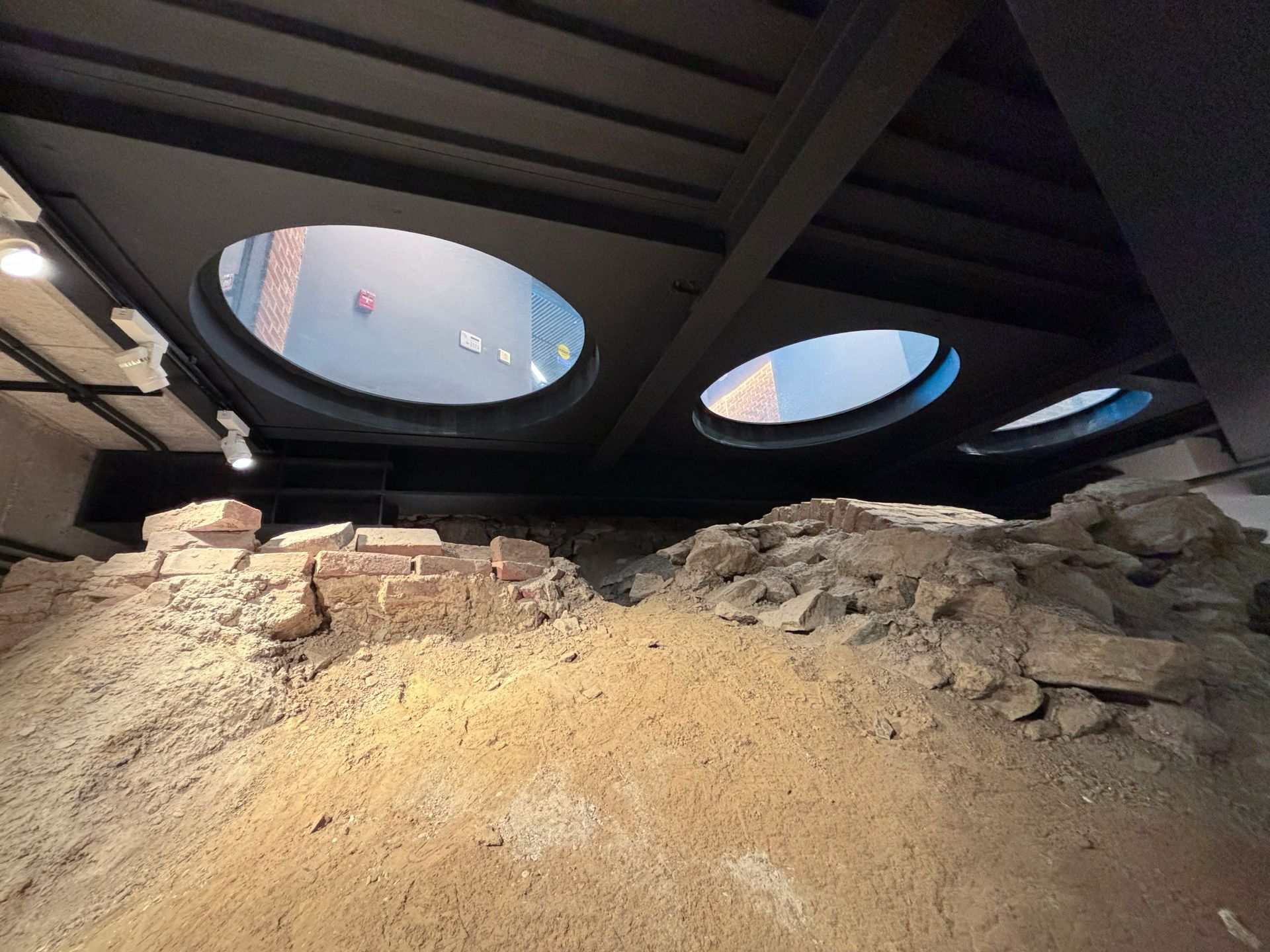 Excavated brick and stone ruins under a dark ceiling with circular skylights.