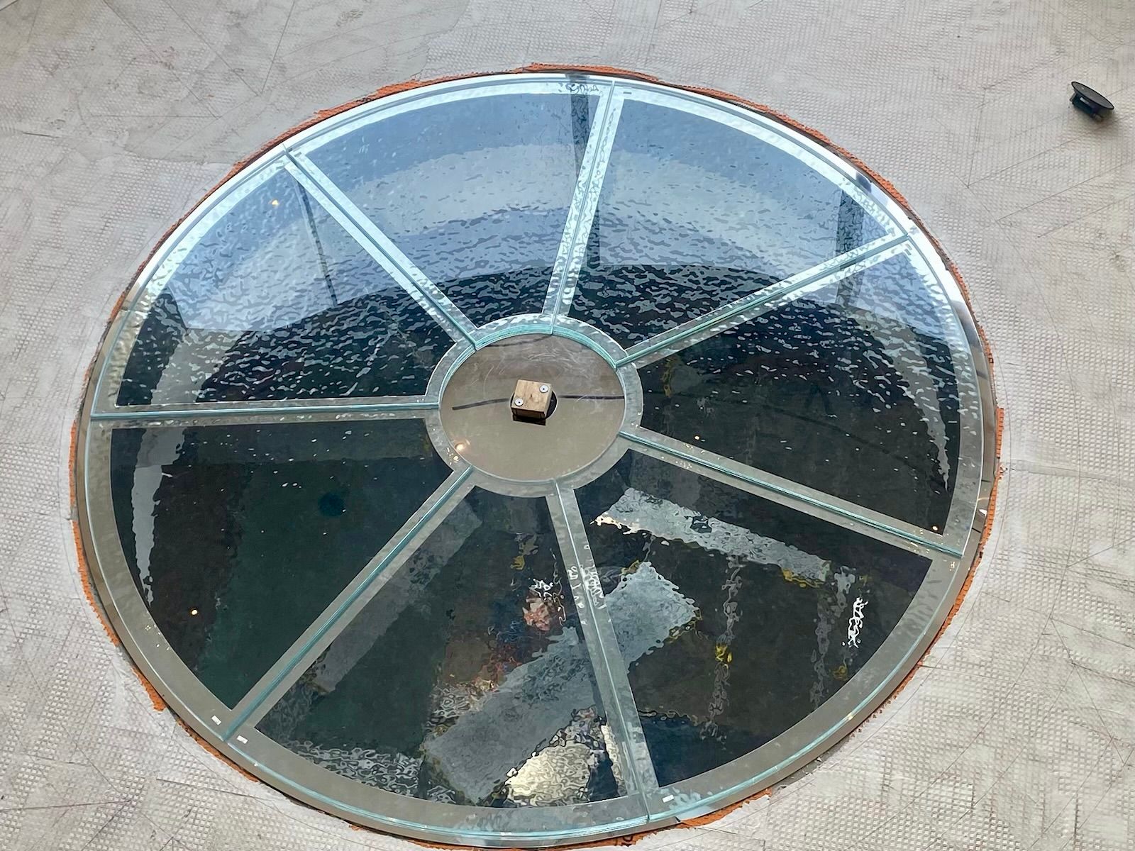 A circular glass skylight inset into a flat, textured roof, featuring a radial metal frame pattern.
