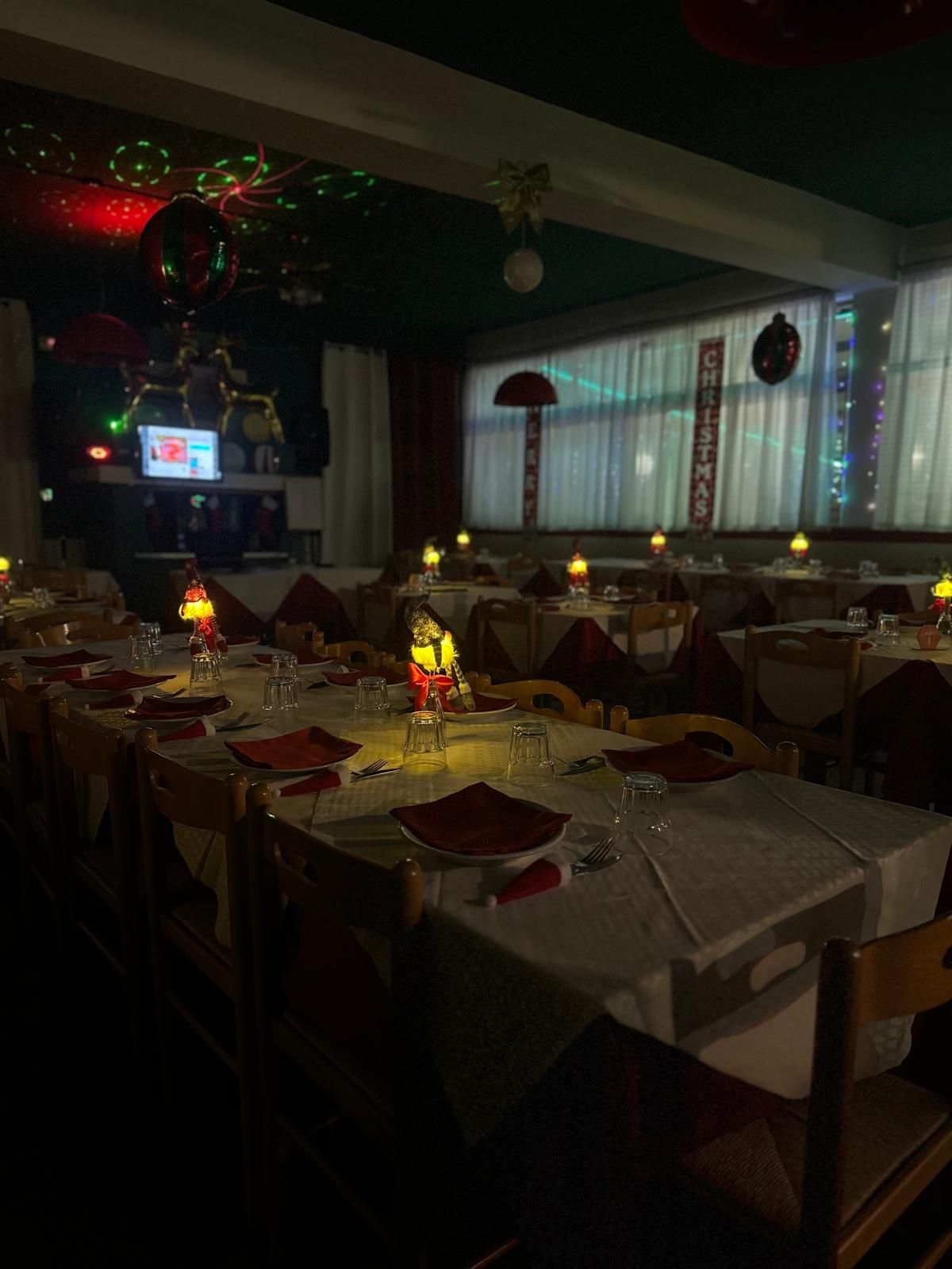 Una sala da pranzo apparecchiata per la cena con tovaglie bianche, tovaglioli rossi e lampade da tavolo scintillanti sotto le luci festive delle vacanze.