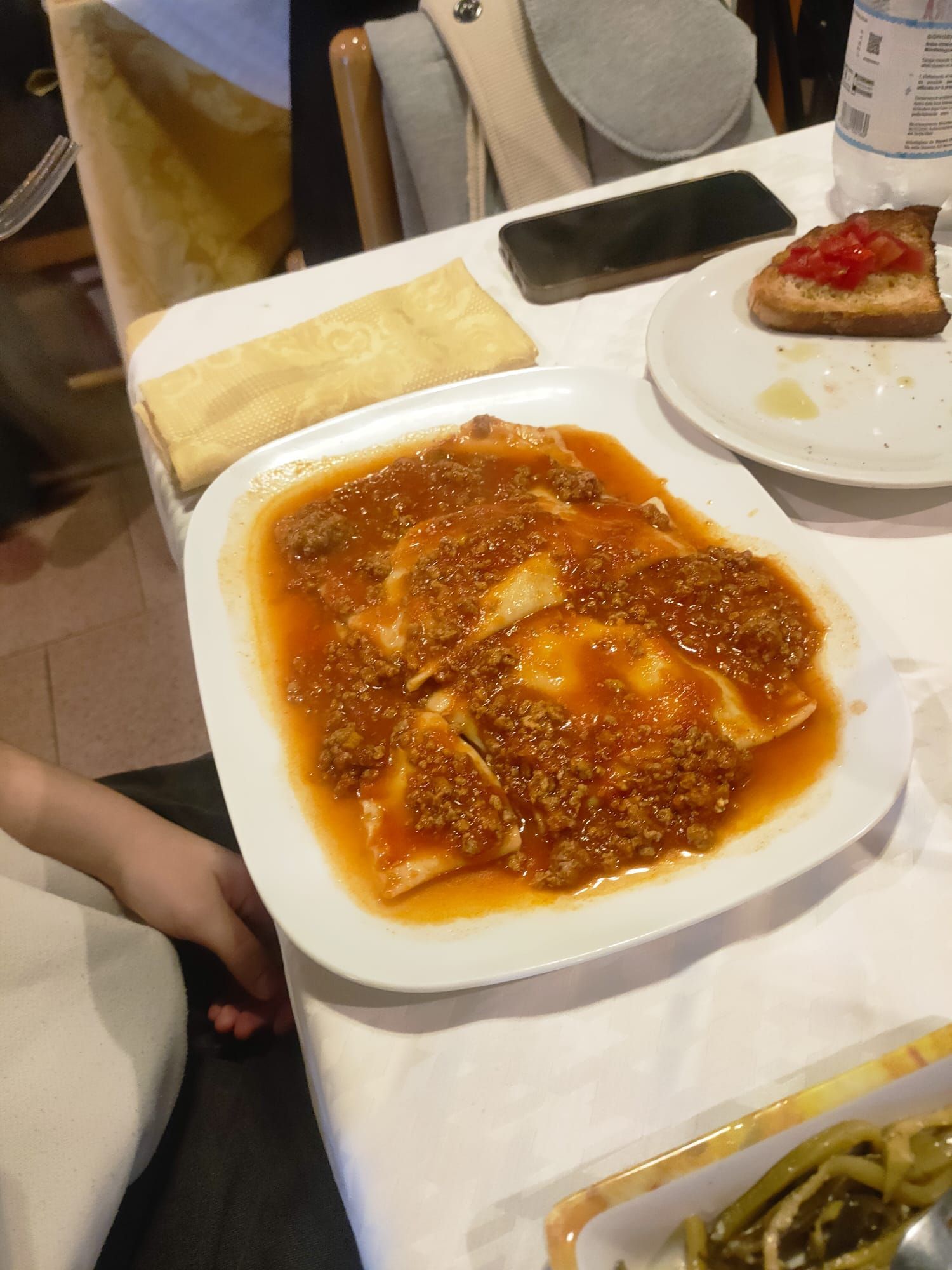 Primo piano di un piatto di ravioli al ragù, servito su una tovaglia bianca con una bruschetta a lato.