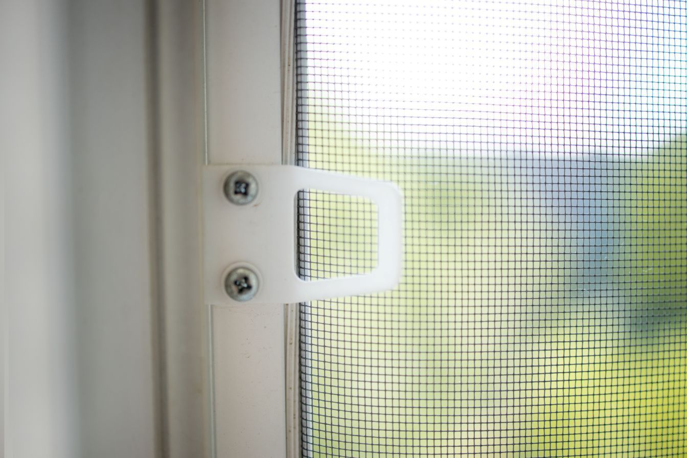 Close-up of a white screen window handle, attached with two screws, against the window screen.
