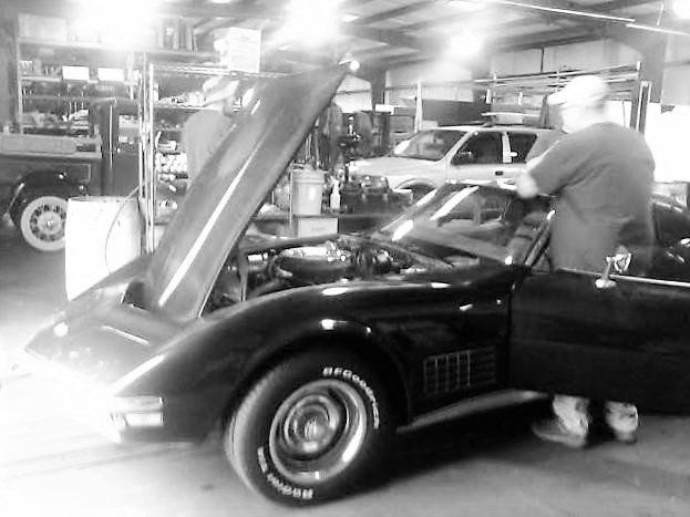 A man is working on a black corvette in a garage.