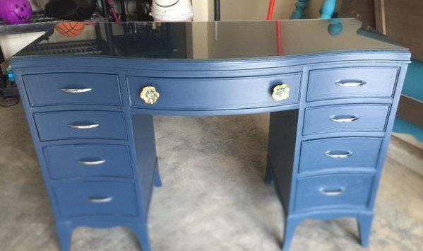 A blue desk with drawers and a glass top is sitting in a garage.