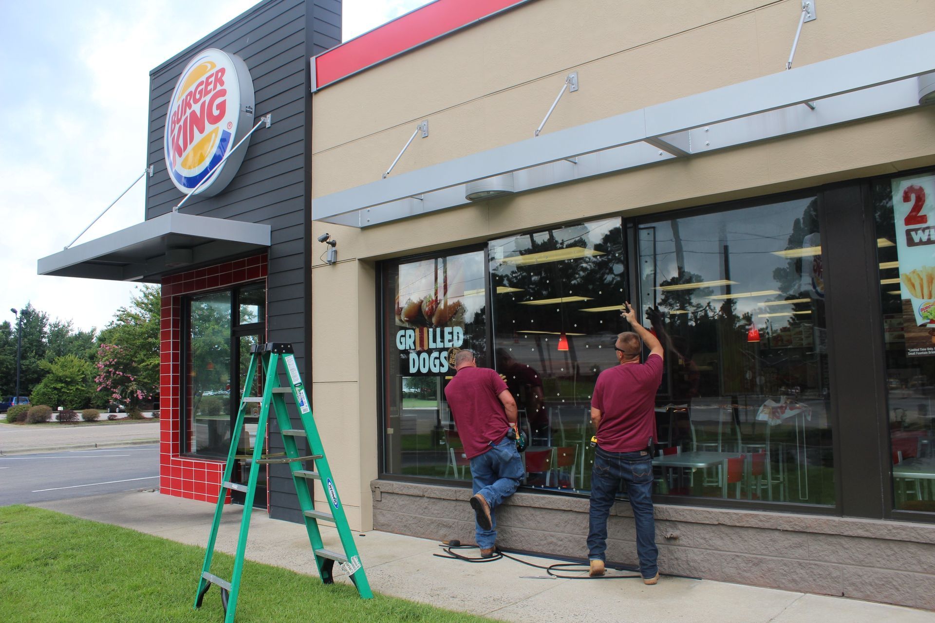 Two men are working on the windows of a burger king restaurant.
