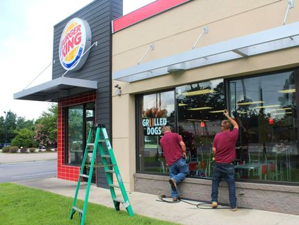 Two men are cleaning the windows of a burger king restaurant