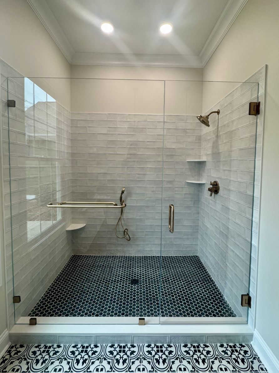 Modern shower with glass doors, gray and white tile walls, mosaic floor, bronze fixtures.
