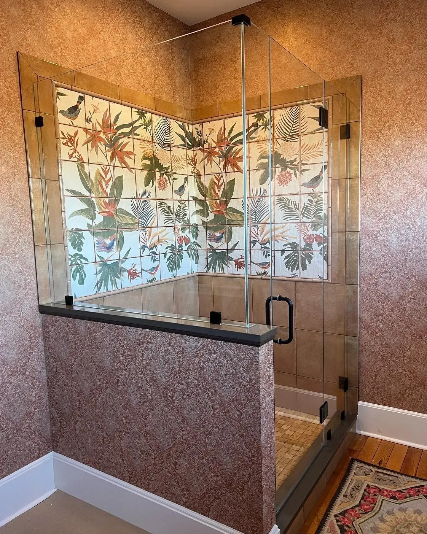 A bathroom with a walk in shower with a floral wallpaper on the wall.